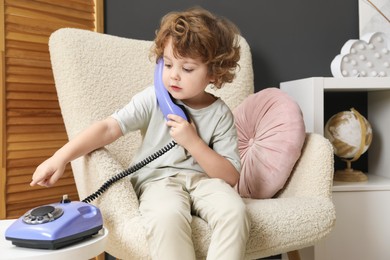 Photo of Cute little boy with telephone in armchair indoors