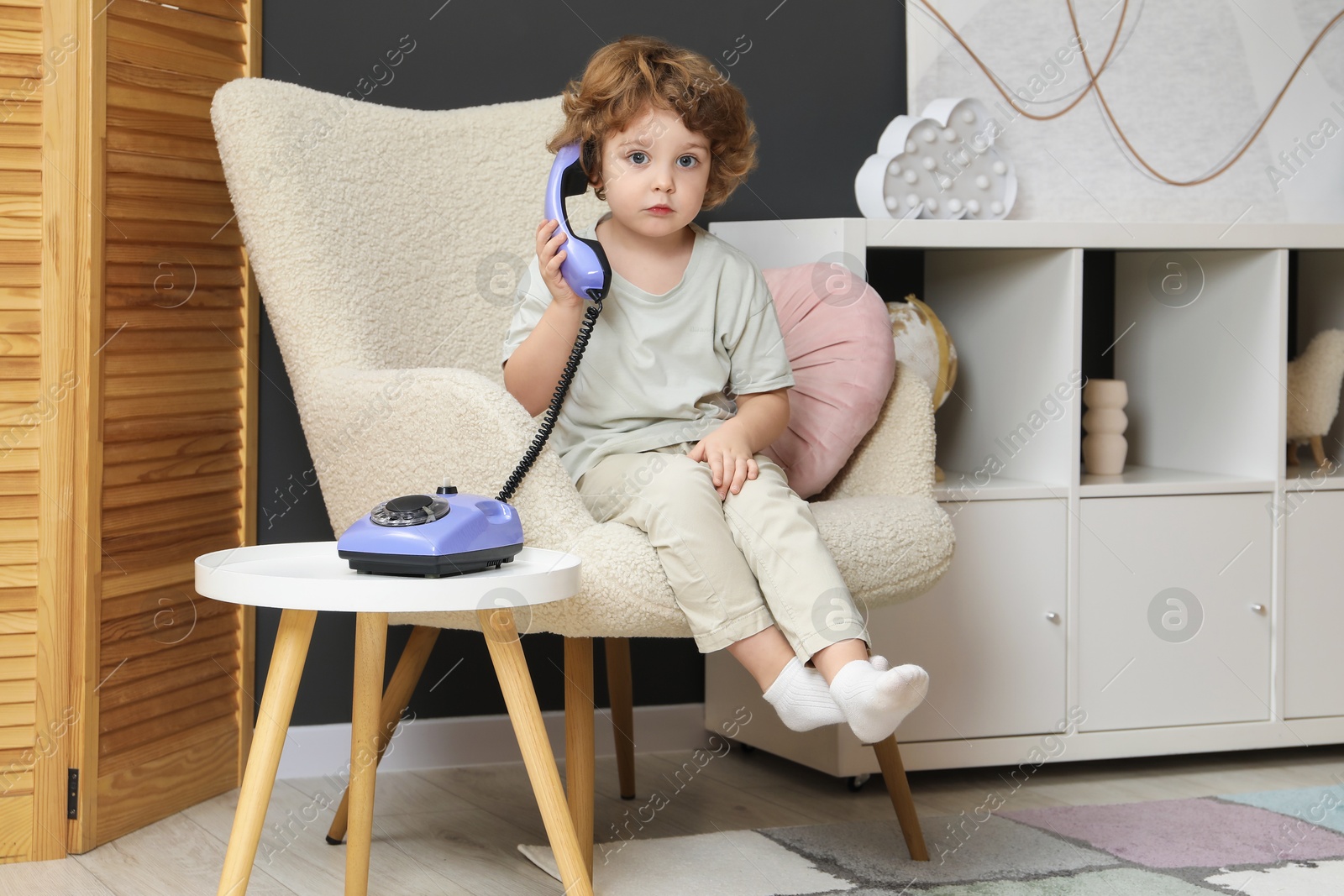 Photo of Cute little boy with telephone in armchair indoors