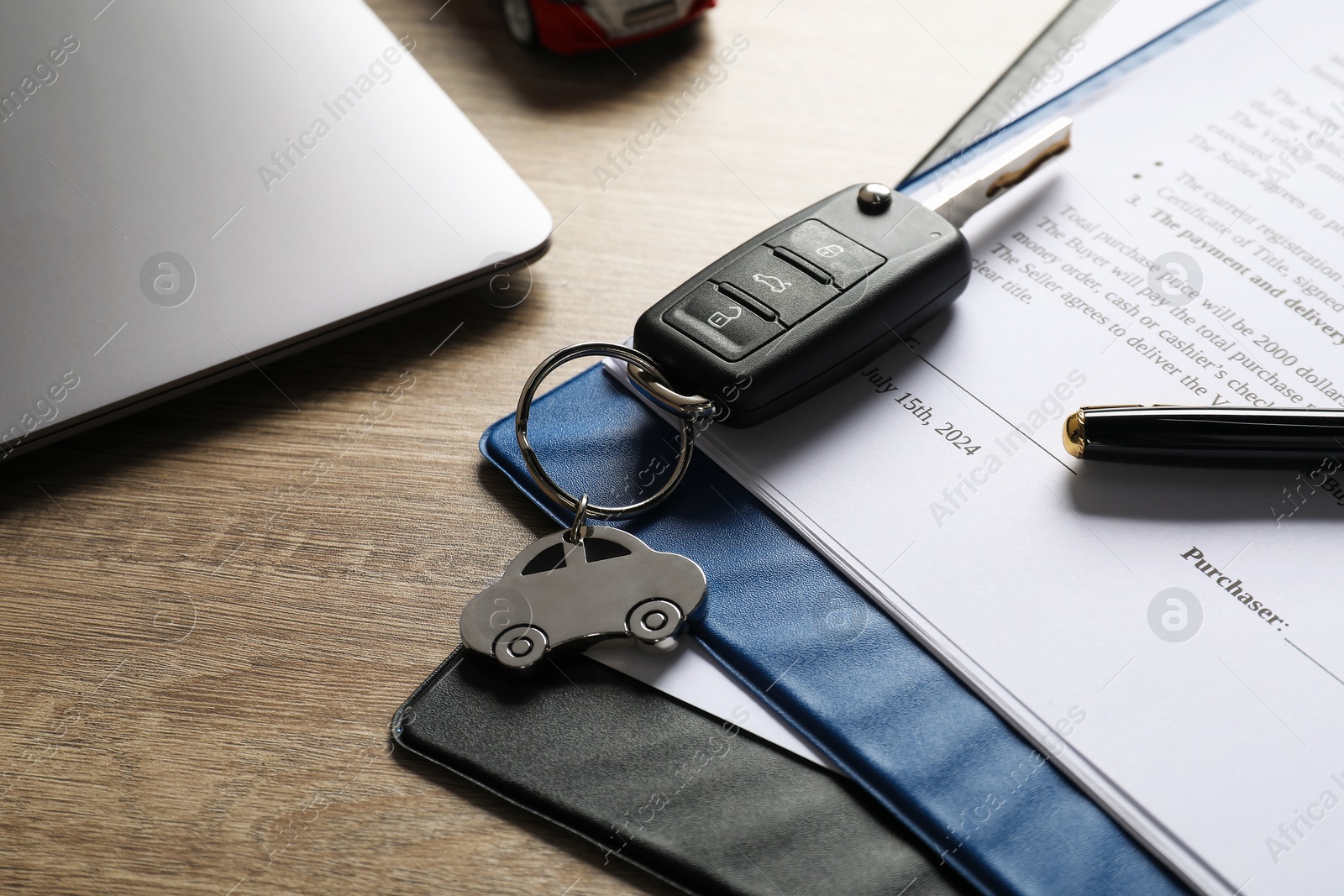 Photo of Car key, purchase agreement and laptop on wooden table, closeup. Buying auto