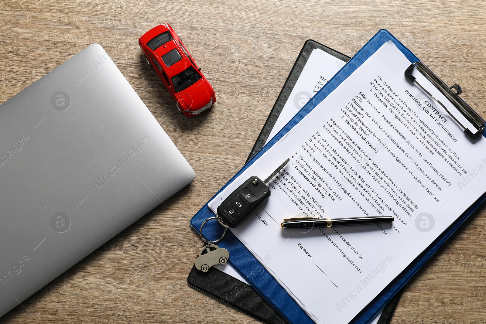 Photo of Car key, model, purchase agreement and laptop on wooden table, flat lay. Buying auto