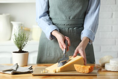 Photo of Woman cutting delicious cheese with slicer at wooden table indoors, closeup