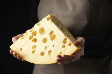 Photo of Woman with piece of delicious cheese on black background, closeup