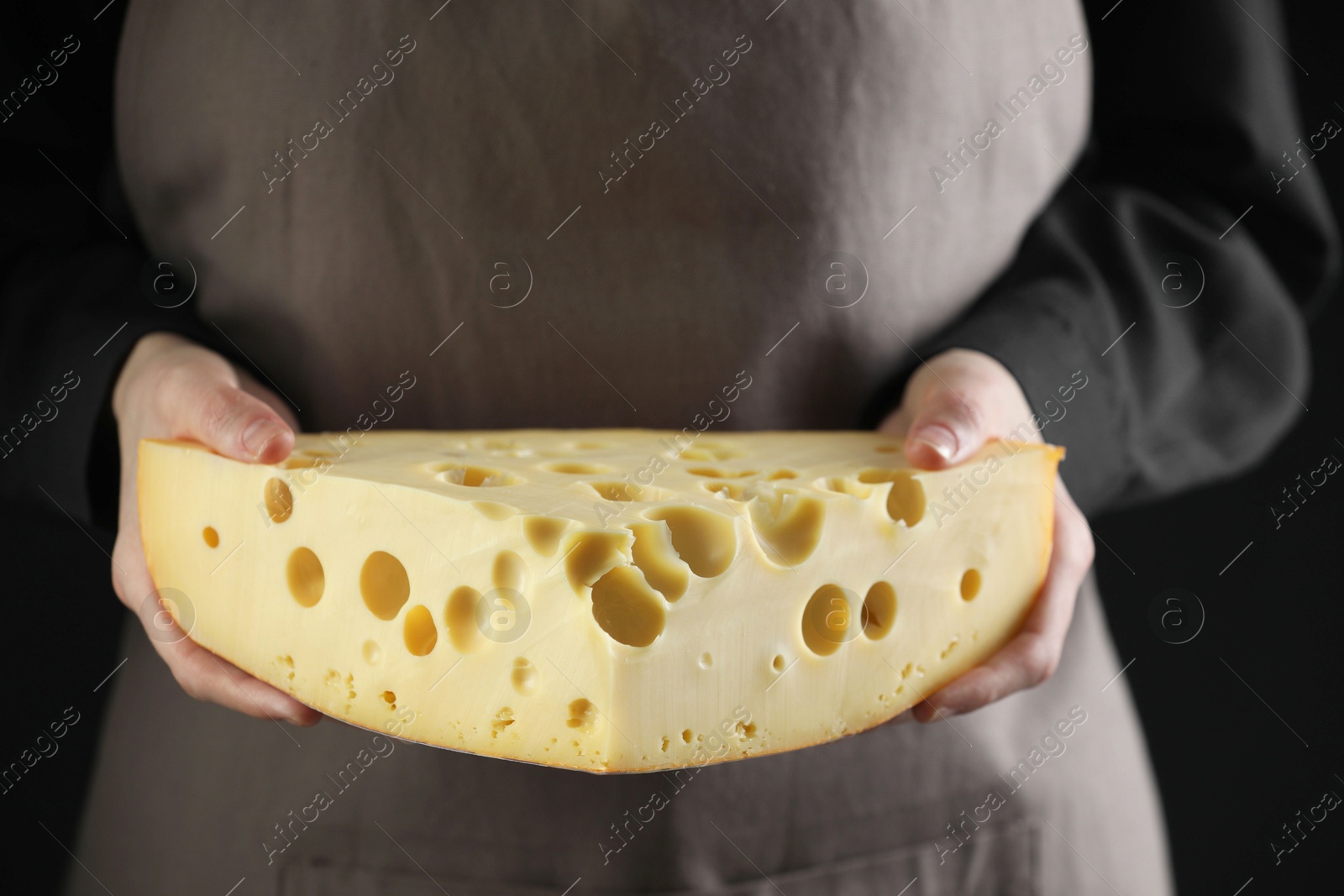 Photo of Woman with piece of delicious cheese on black background, closeup