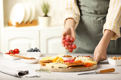 Photo of Woman serving antipasto platter with different types of cheese and other snacks with grapes at grey textured table indoors, closeup. Space for text