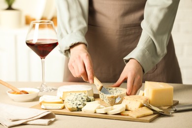 Photo of Woman slicing delicious cheese at light textured table indoors, closeup