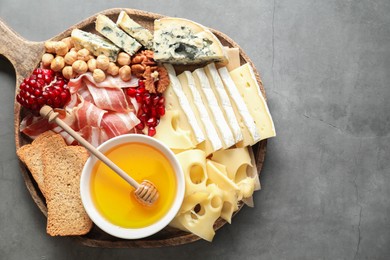 Photo of Different types of cut cheese and other snacks on gray textured table, top view. Space for text