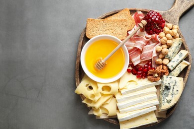 Photo of Different types of cut cheese and other snacks on gray textured table, top view. Space for text