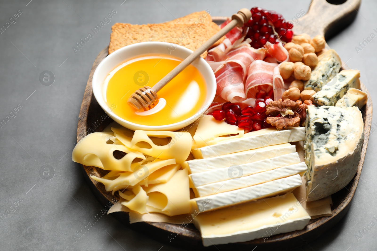 Photo of Different types of cut cheese and other snacks on gray textured table, closeup