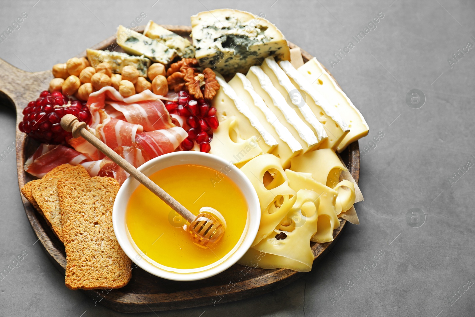 Photo of Different types of cut cheese and other snacks on gray textured table, closeup