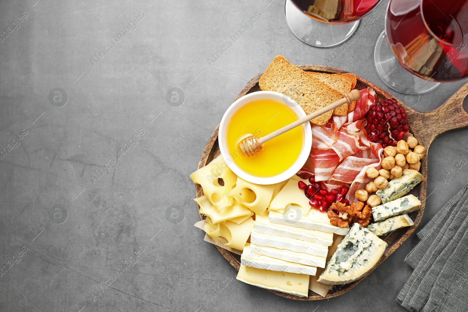 Photo of Different types of cut cheese and other snacks served with wine on gray textured table, flat lay. Space for text