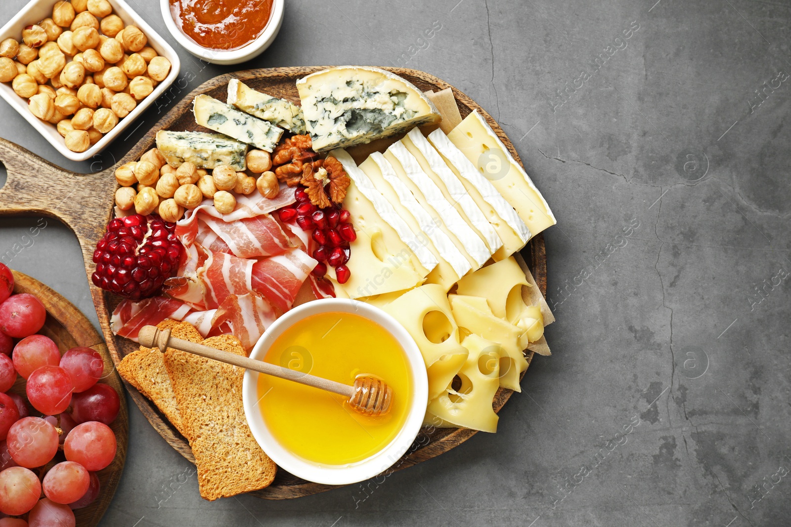 Photo of Different types of cut cheese and other snacks on gray textured table, top view. Space for text