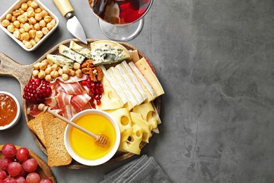 Photo of Different types of cut cheese and other snacks served with wine on gray textured table, flat lay. Space for text