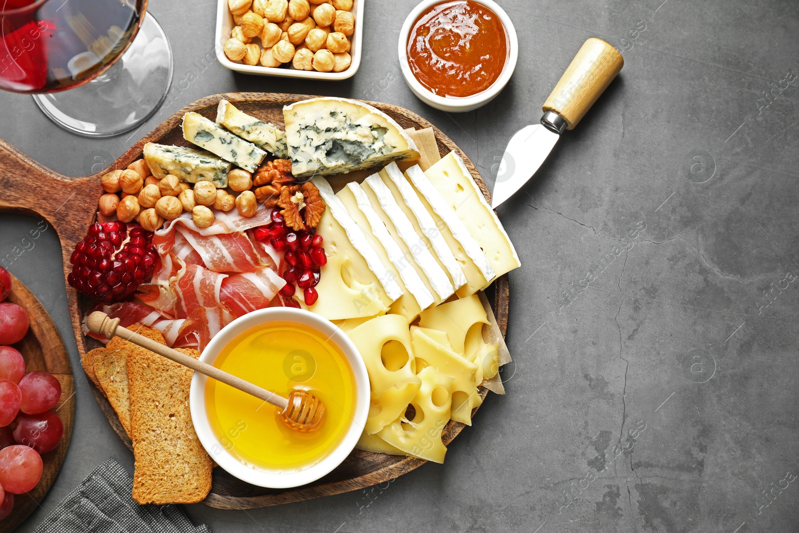 Photo of Different types of cut cheese and other snacks served with wine on gray textured table, flat lay. Space for text