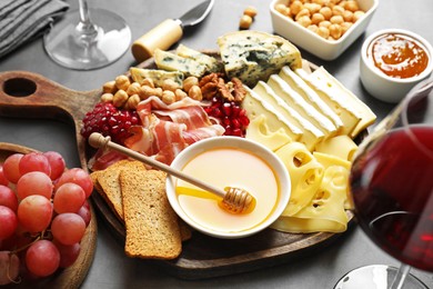 Photo of Different types of cut cheese and other snacks served with wine on gray table, closeup