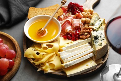 Photo of Different types of cut cheese and other snacks served with wine on gray table, closeup