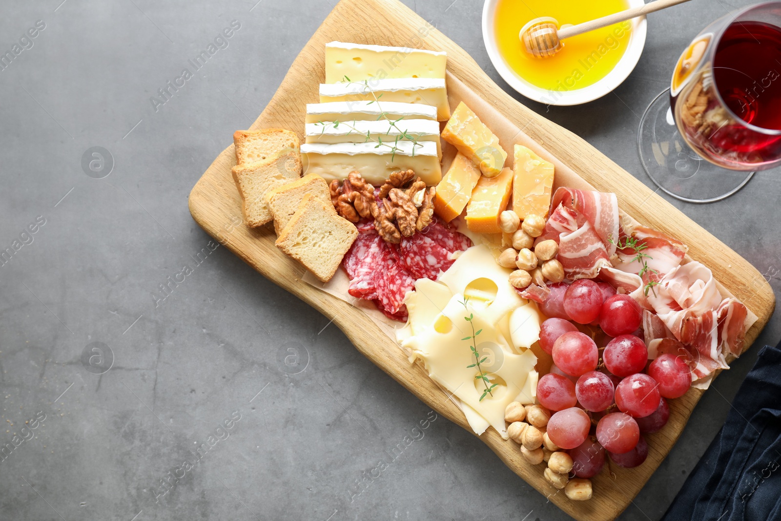 Photo of Different types of cut cheese and other snacks served with wine on gray textured table, flat lay. Space for text