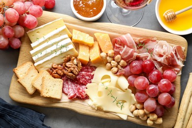 Photo of Different types of cut cheese and other snacks served with wine on gray textured table, flat lay