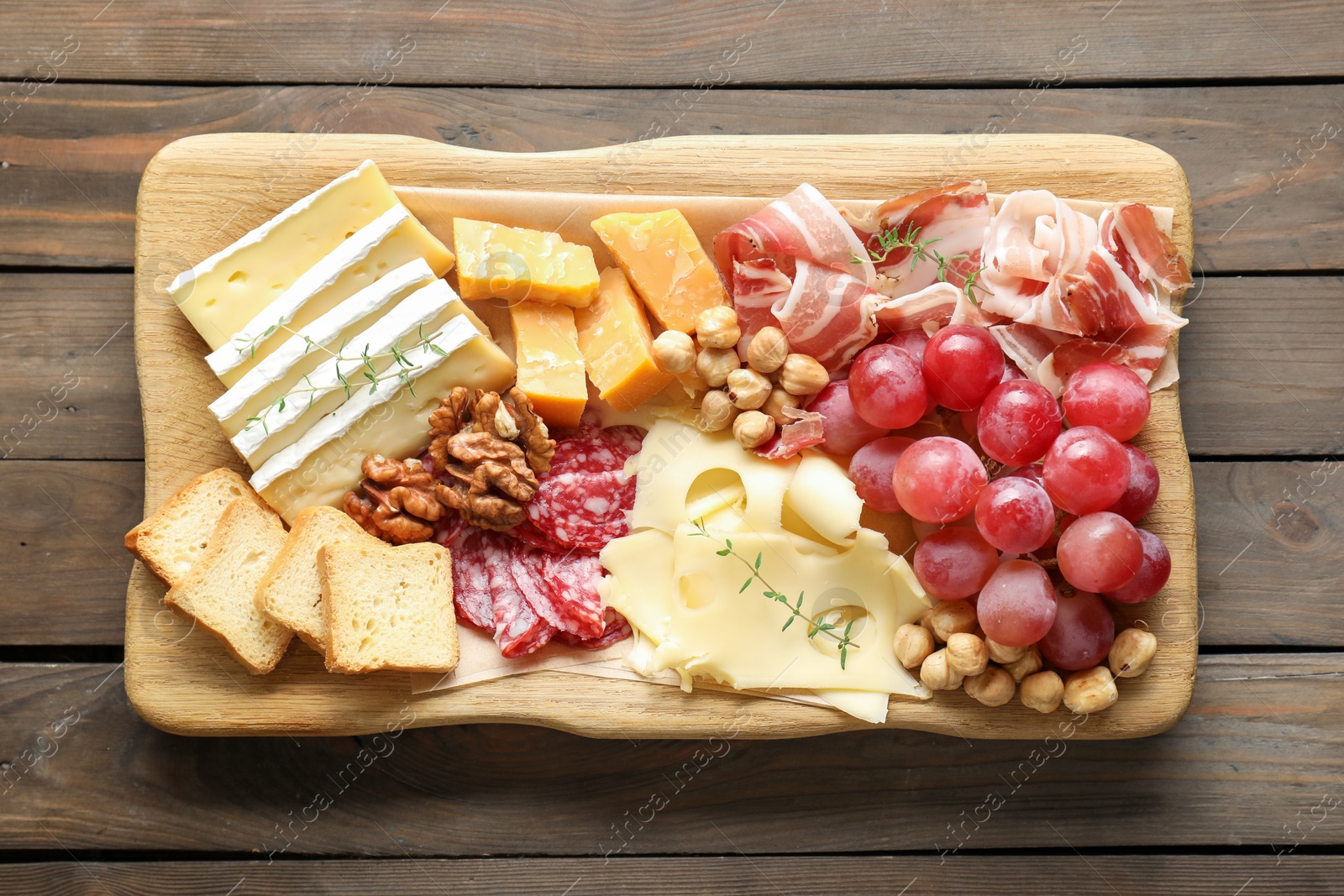 Photo of Different types of cut cheese and other snacks on wooden table, top view