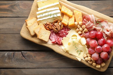 Photo of Different types of cut cheese and other snacks on wooden table, top view