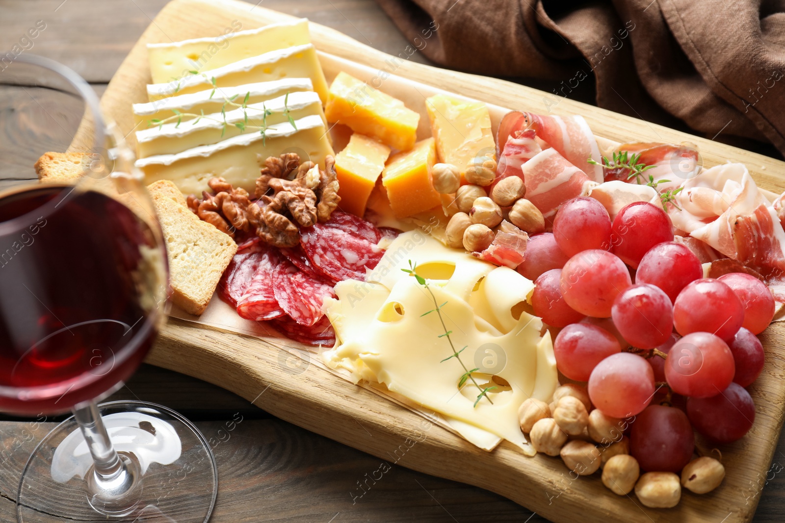 Photo of Different types of cut cheese and other snacks served with wine on wooden table, closeup