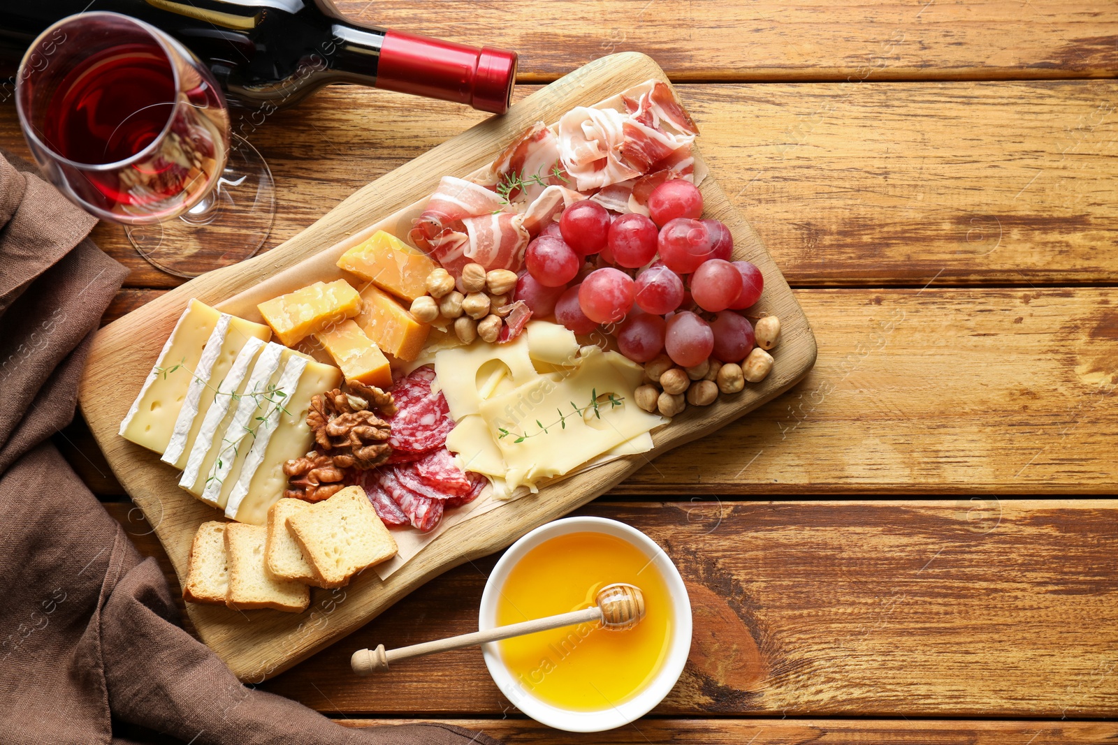 Photo of Different types of cut cheese and other snacks served with wine on wooden table, flat lay. Space for text