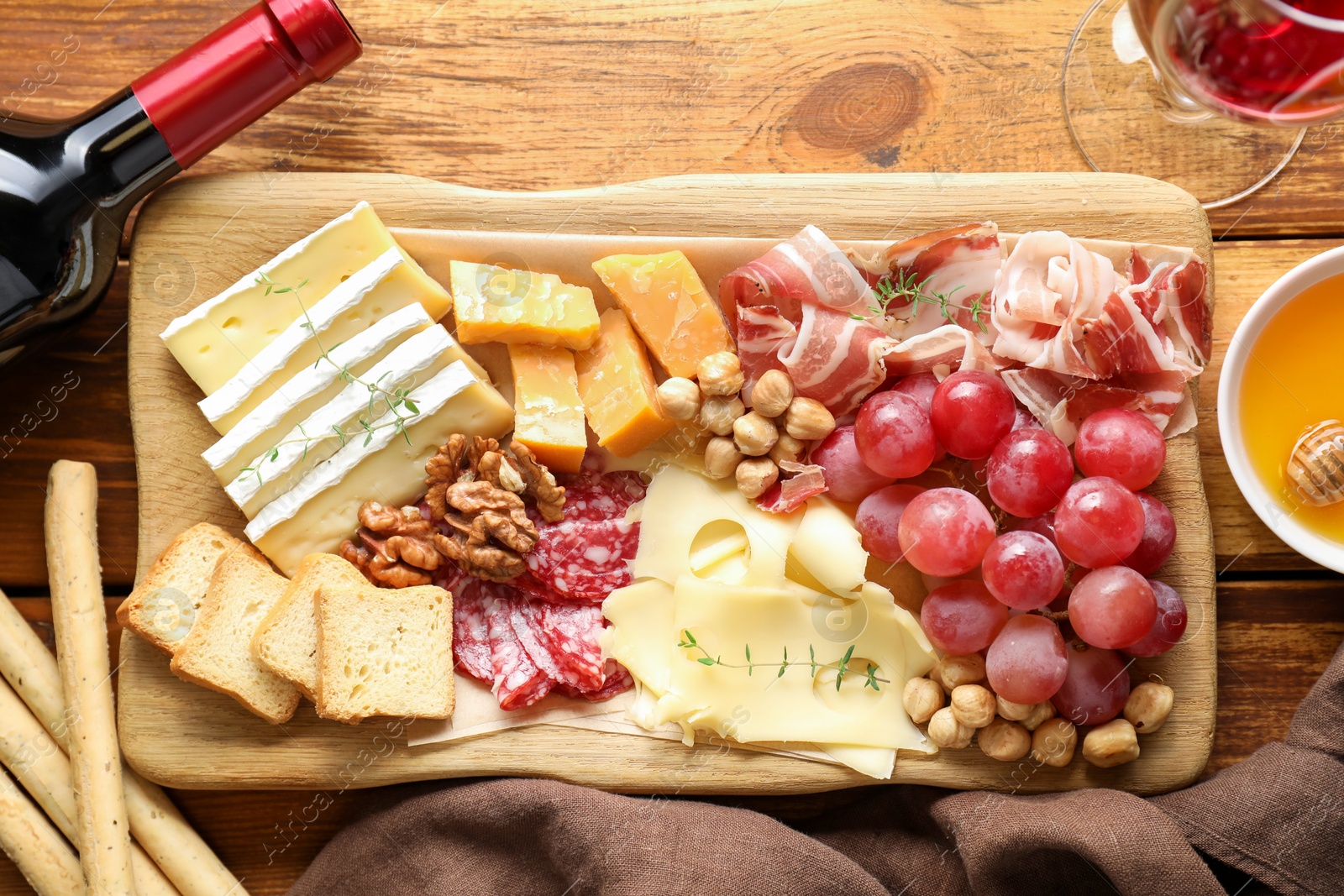 Photo of Different types of cut cheese and other snacks served with wine on wooden table, flat lay