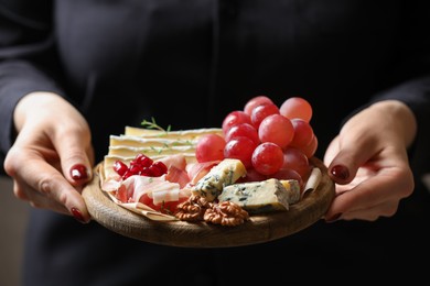 Photo of Woman holding board with different types of delicious cheese and other snacks, closeup