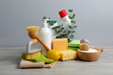 Photo of Eco-friendly cleaning products, supplies and eucalyptus branches on wooden table against grey background