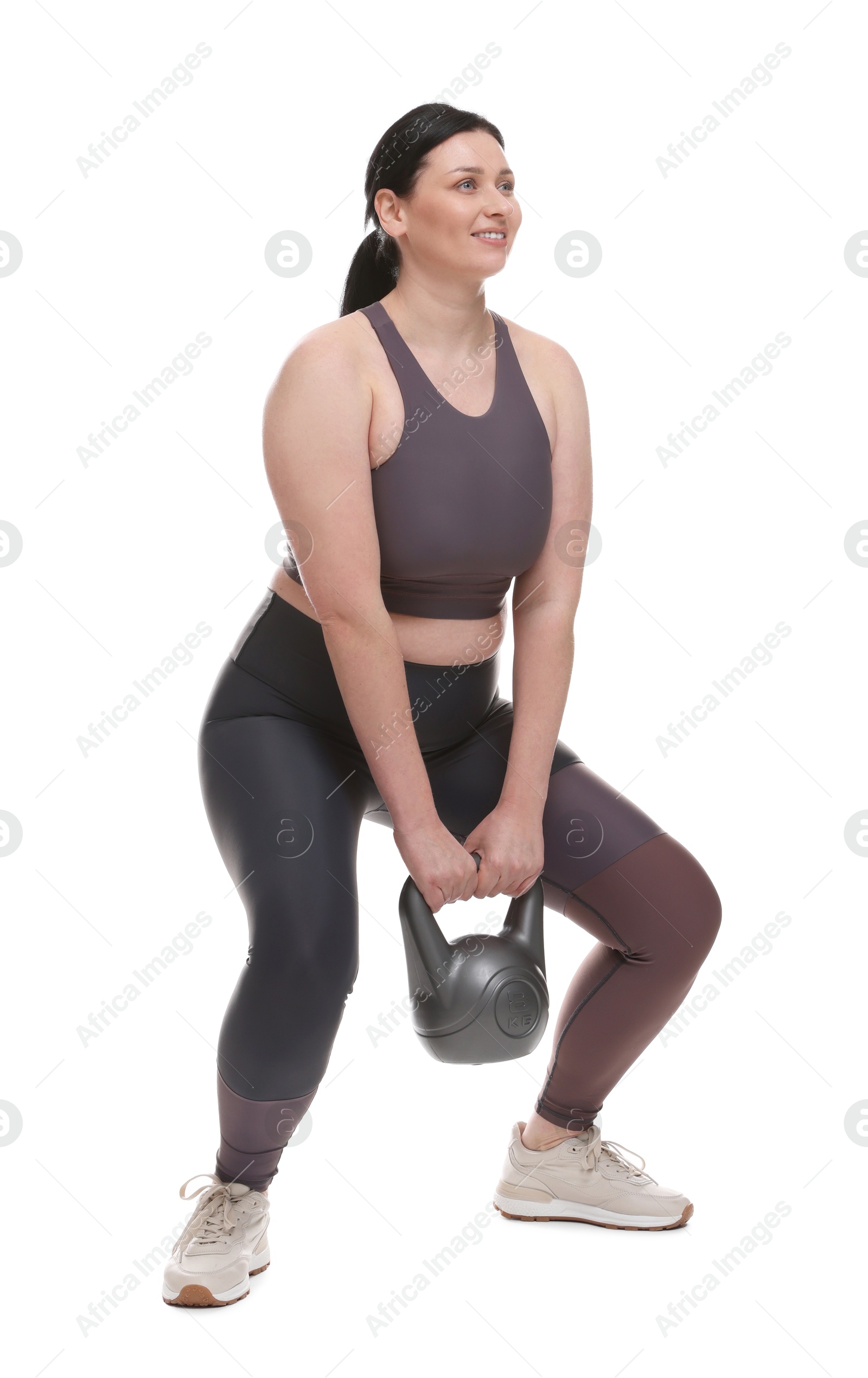 Photo of Plus size woman in gym clothes doing exercise with kettlebell on white background