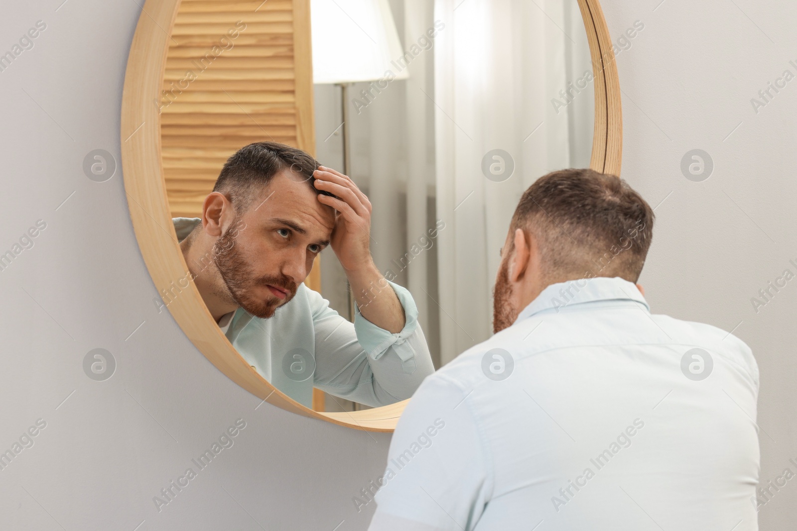 Photo of Baldness problem. Man with receding hairline near mirror at home, back view