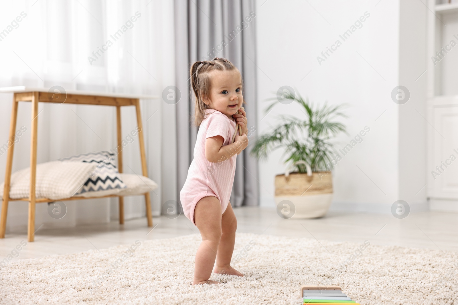 Photo of First steps. Cute little baby with drumsticks learning to walk at home