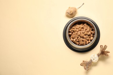 Wet pet food in feeding bowl and cat toys on pale yellow background, flat lay. Space for text