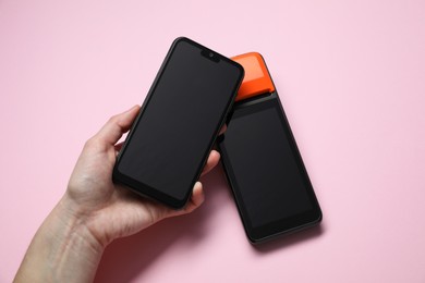 Photo of Woman with smartphone using payment terminal on pink background, top view