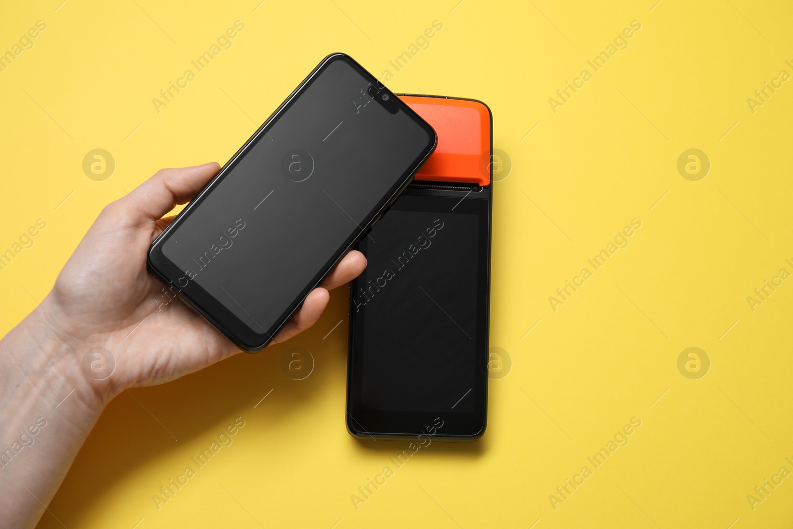 Photo of Woman with smartphone using payment terminal on yellow background, top view