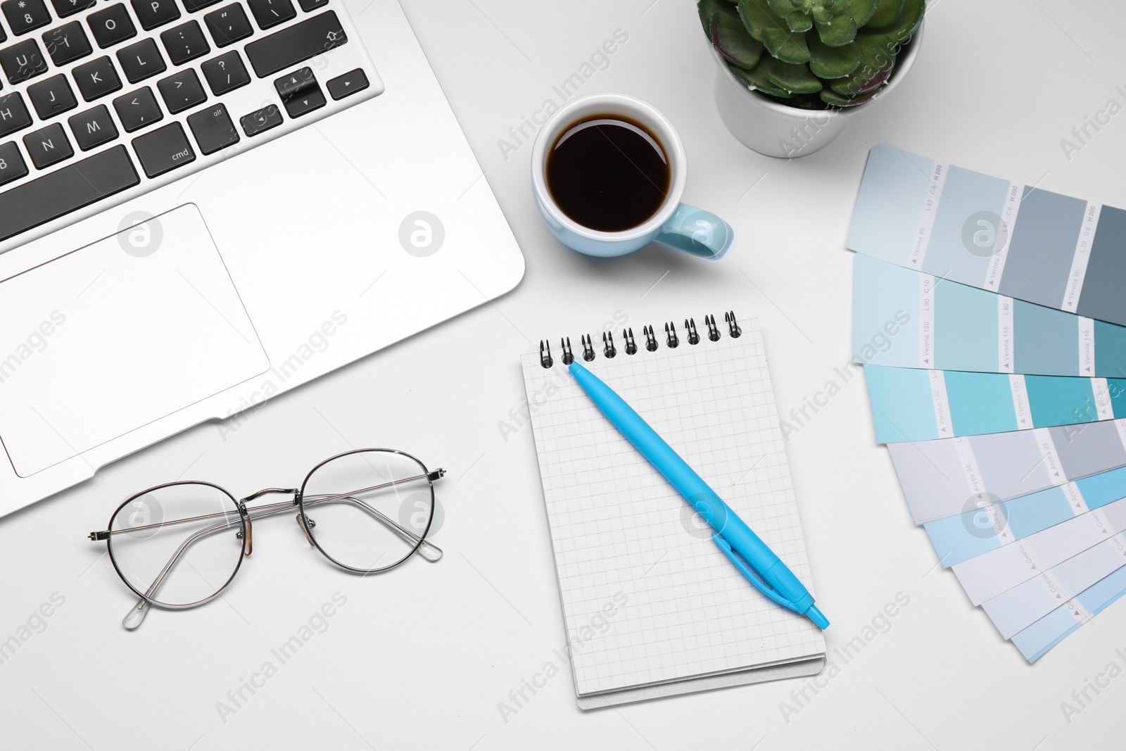 Photo of Designer's workplace with stationery, color palettes, cup of coffee and laptop on grey table, flat lay