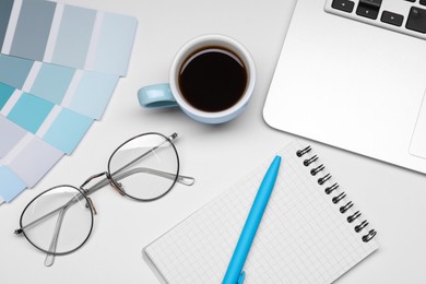 Photo of Designer's workplace with stationery, color palettes, cup of coffee and laptop on grey table, flat lay