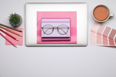 Photo of Designer's workplace with stationery, color palettes, tea and laptop on grey table, flat lay. Space for text