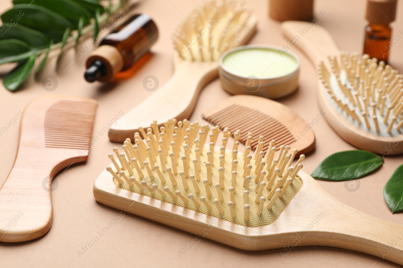 Photo of Wooden hair brushes, combs, cosmetic products and green leaves on dark beige background, closeup