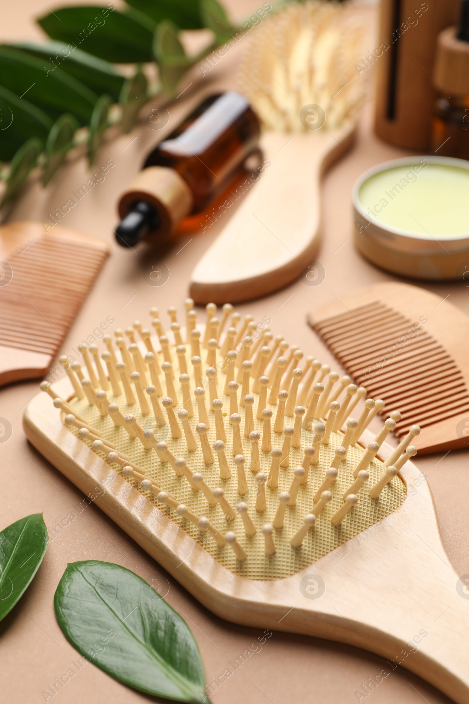 Photo of Wooden hair brushes, combs, cosmetic products and green leaves on dark beige background, closeup