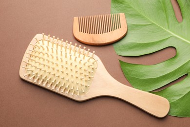 Photo of Wooden hair brush, comb and monstera leaf on dark beige background, flat lay