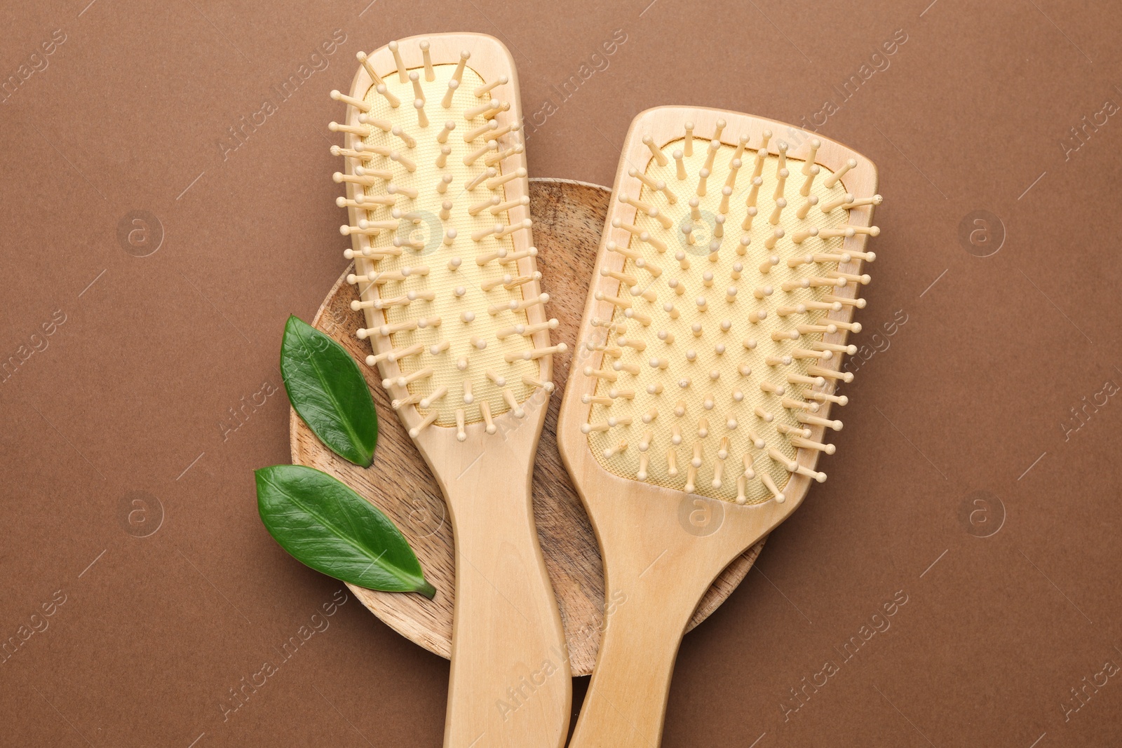 Photo of Wooden hair brushes and green leaves on dark beige background, top view