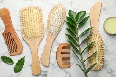 Photo of Wooden hair brushes, combs, wax and green leaves on white marble table, flat lay