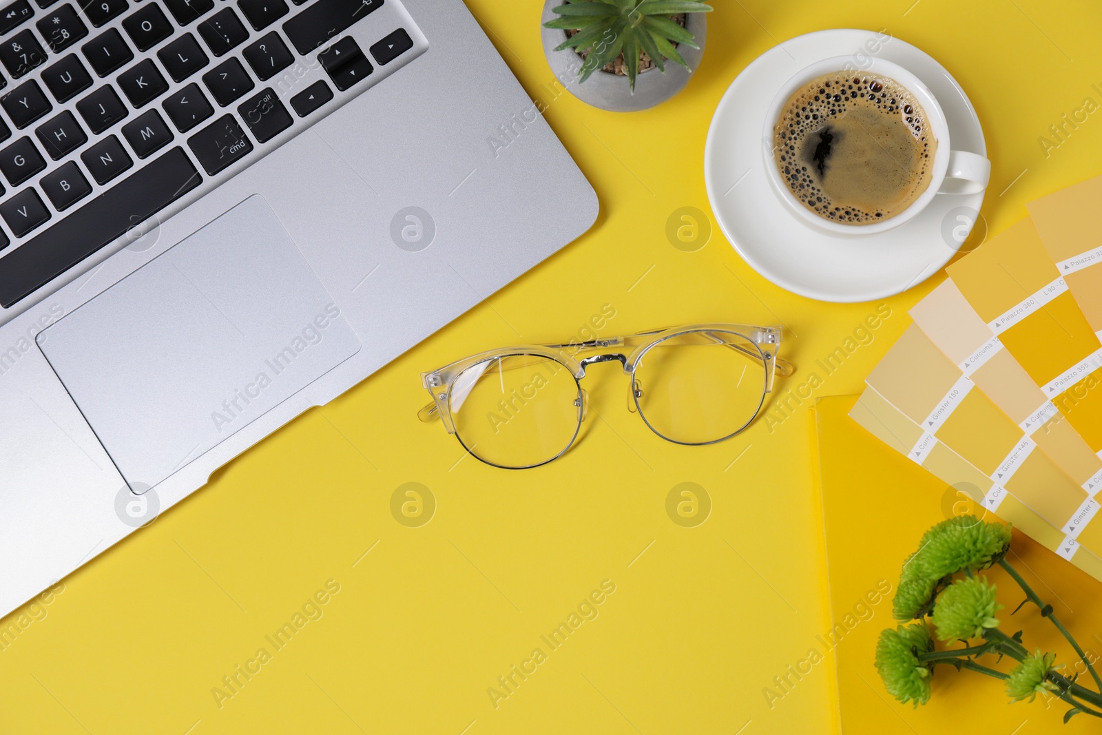 Photo of Designer's workplace with laptop, stationery and cup of coffee on yellow background, flat lay