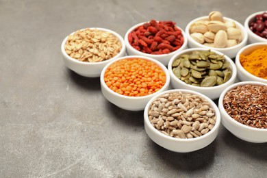 Photo of Different superfoods in bowls on grey table, closeup. Space for text