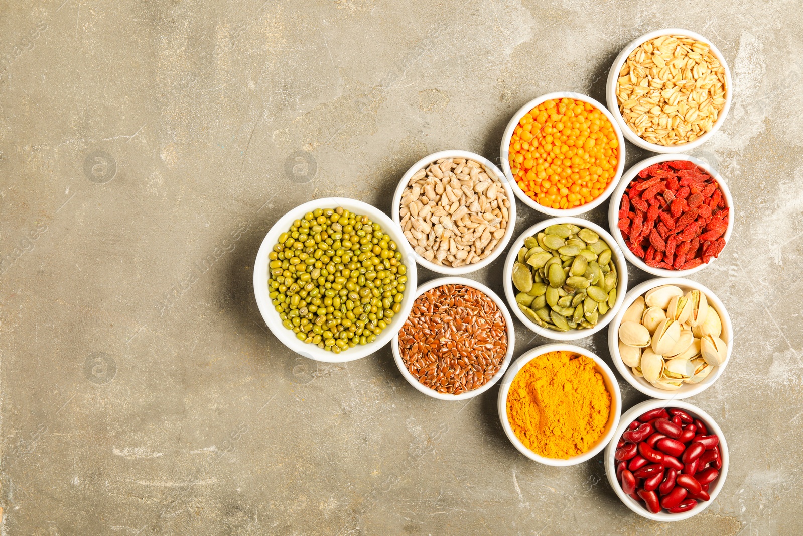 Photo of Different superfoods in bowls on grey table, flat lay. Space for text