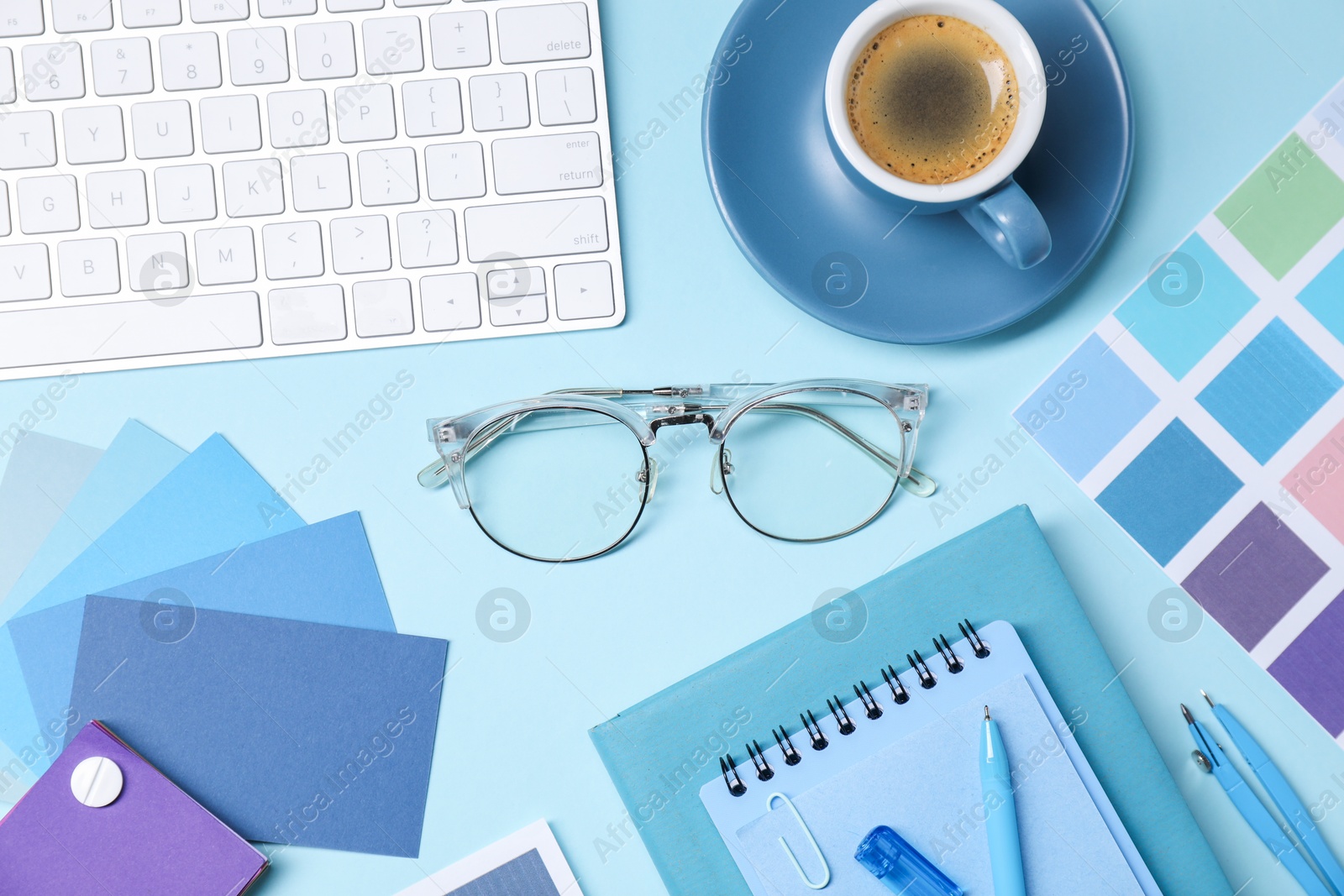 Photo of Designer's workplace. Flat lay composition with stationery and keyboard on light blue background