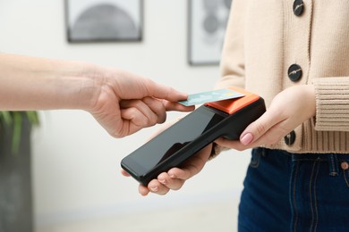 Photo of Woman paying for service with credit card via terminal indoors, closeup