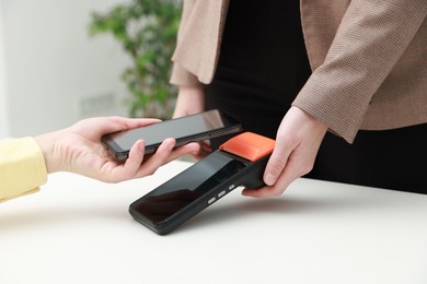 Photo of Woman paying for service with smartphone via terminal at white table indoors, closeup