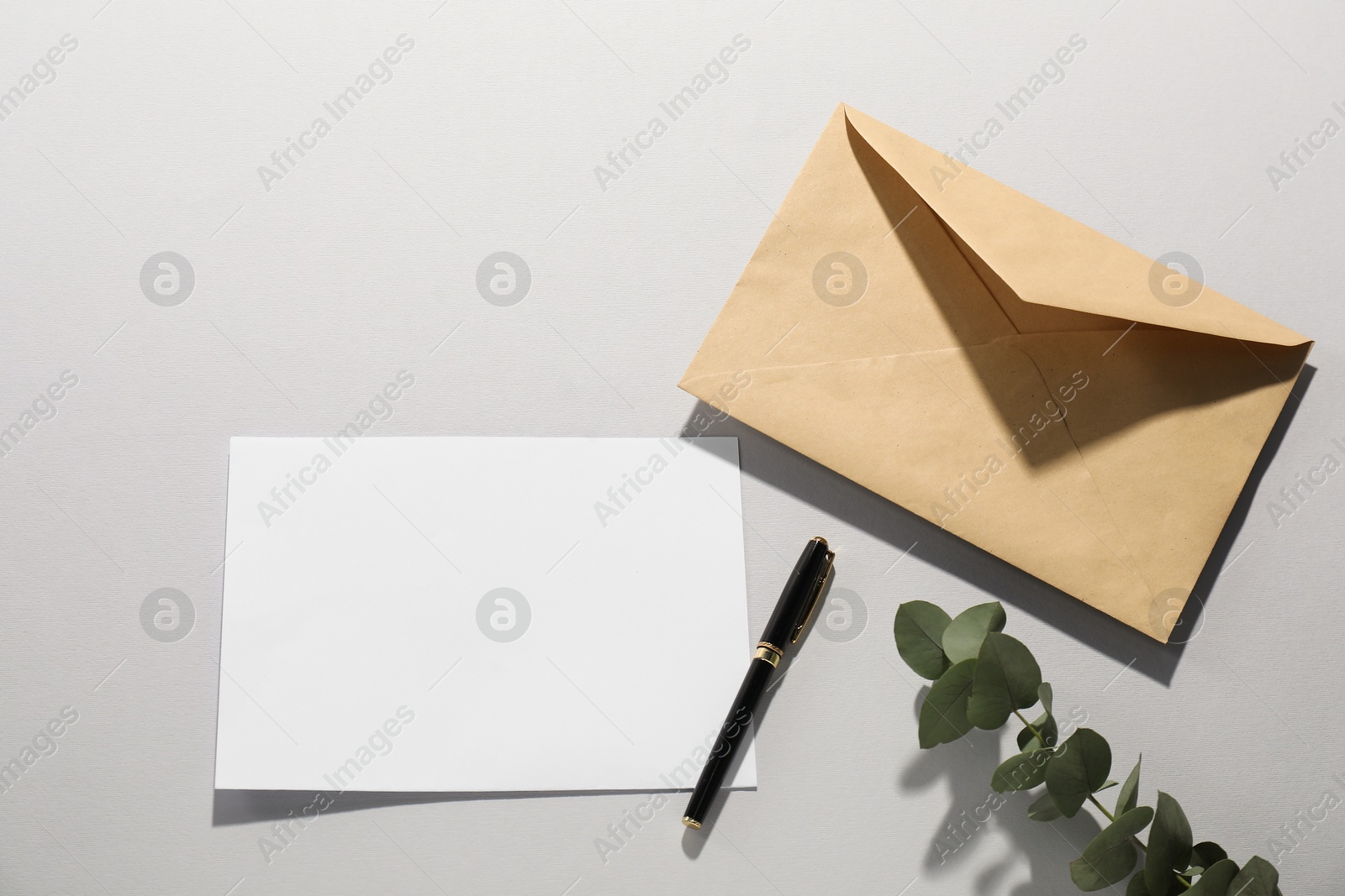 Photo of Kraft paper envelope, letter, pen and eucalyptus branch on grey background, flat lay. Mockup for design