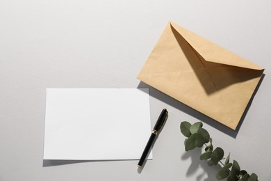 Photo of Kraft paper envelope, letter, pen and eucalyptus branch on grey background, flat lay. Mockup for design